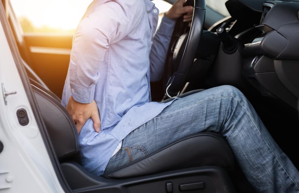 Man experiencing lower back pain after a car accident, possibly suffering from a soft tissue injury