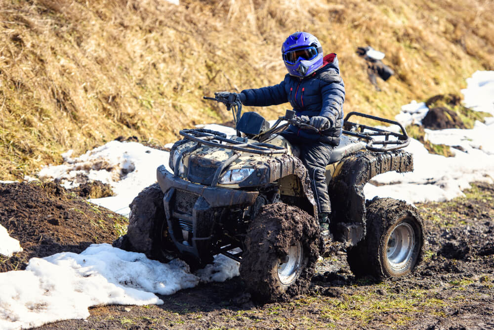Child riding an ATV on a muddy trail in British Columbia wearing full safety gear and helmet
