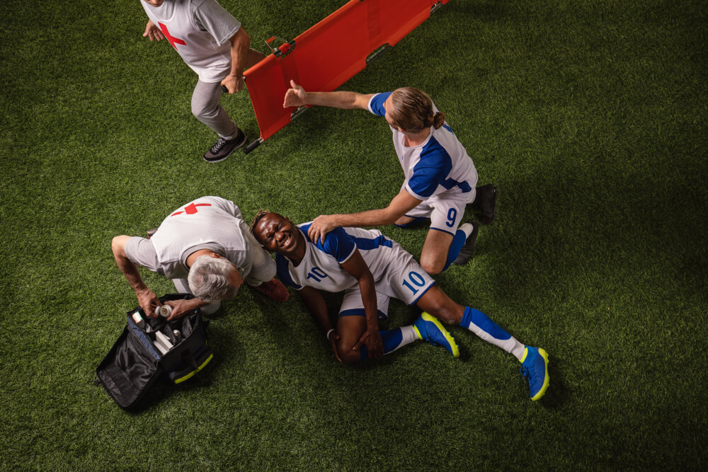 Injured soccer player receiving medical help on the field after a collision, illustrating common soccer and football injuries and potential liability in BC.
