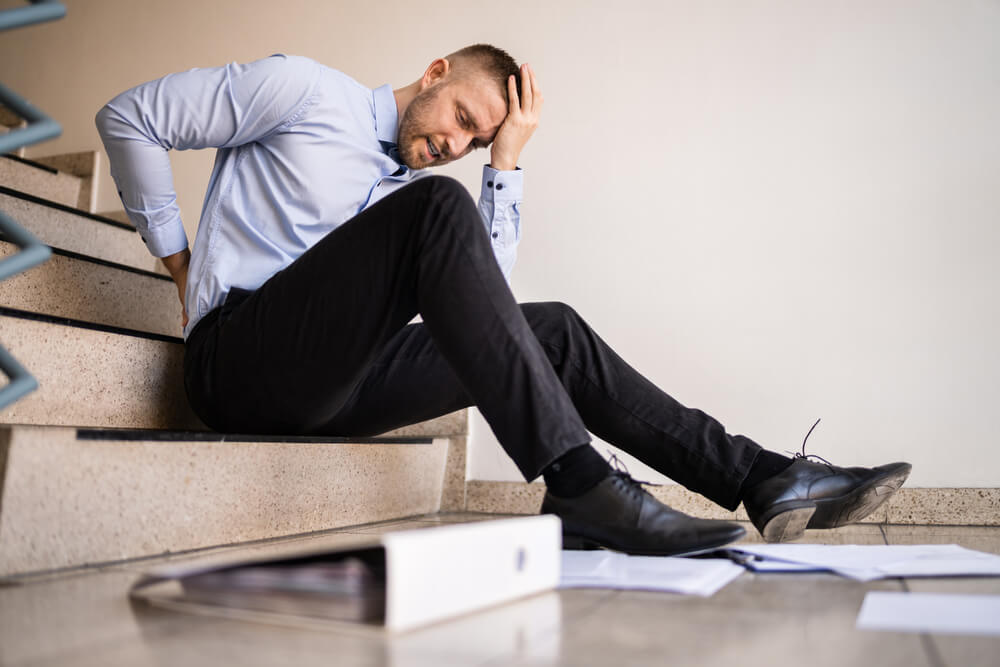 Man sitting on stairs holding his head and back after a fall, showing possible concussion symptoms.