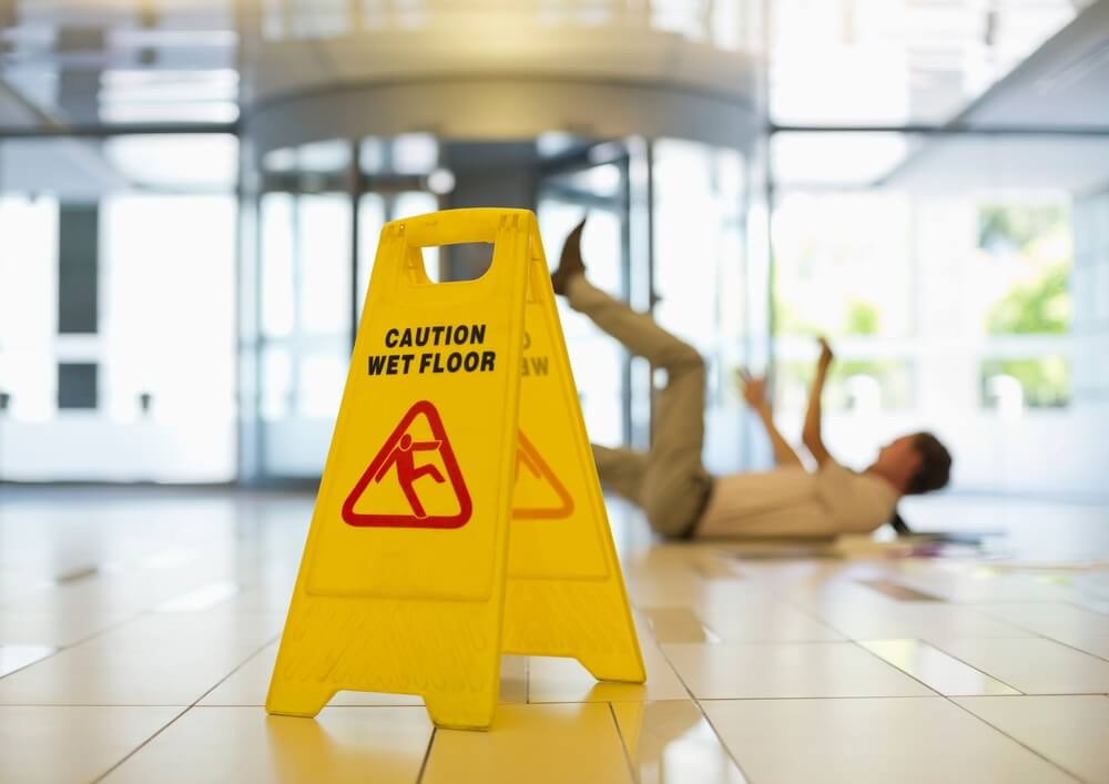 Person slipping beside a wet floor caution sign in a commercial property, illustrating slip and fall negligence in BC.